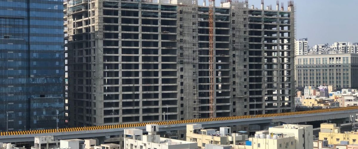 High-rise building under construction in a bustling city with cranes and urban infrastructure.